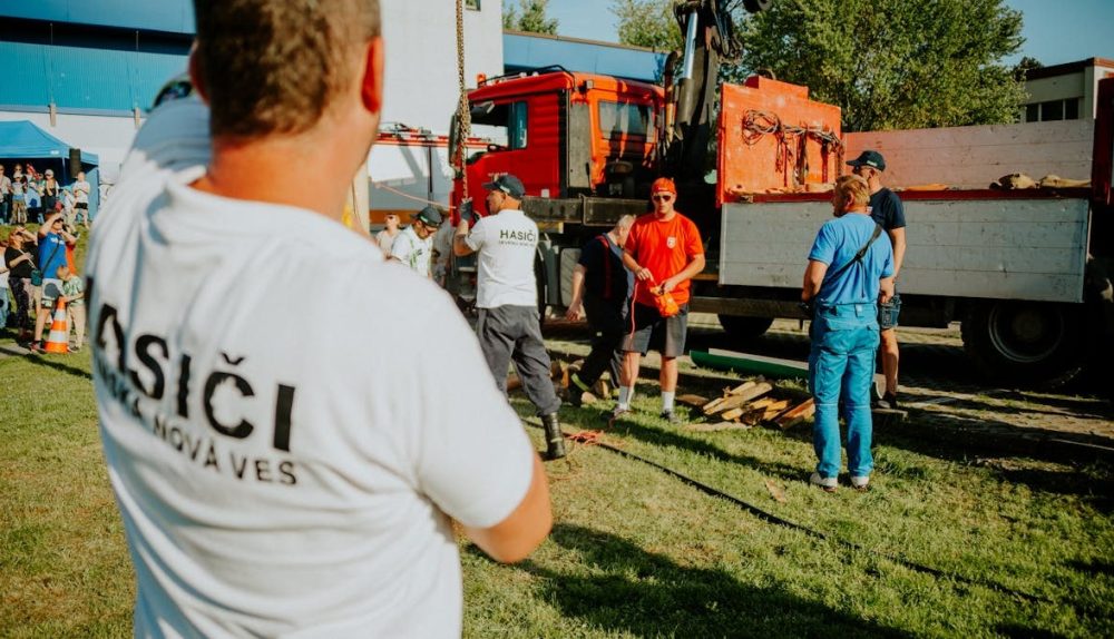 A group of firefighters in a park setting during a public demonstration near a fire truck.