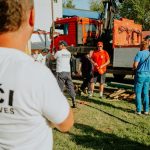 A group of firefighters in a park setting during a public demonstration near a fire truck.