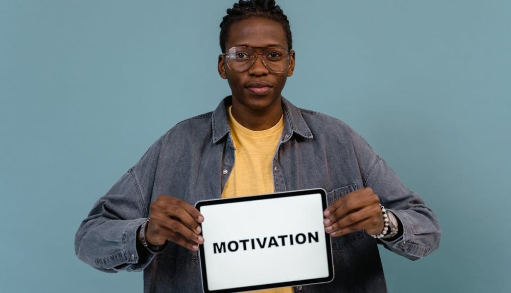 A young African American man holding a tablet displaying the word 'MOTIVATION' against a blue background.
