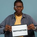 A young African American man holding a tablet displaying the word 'MOTIVATION' against a blue background.