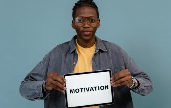 A young African American man holding a tablet displaying the word 'MOTIVATION' against a blue background.